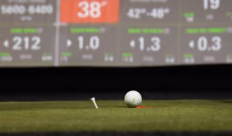 Golf ball on red dot near tee on turf in front of sim screen. 