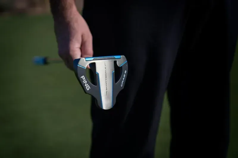 Close-up of a PING Scottsdale putter head with golf pants in the background.