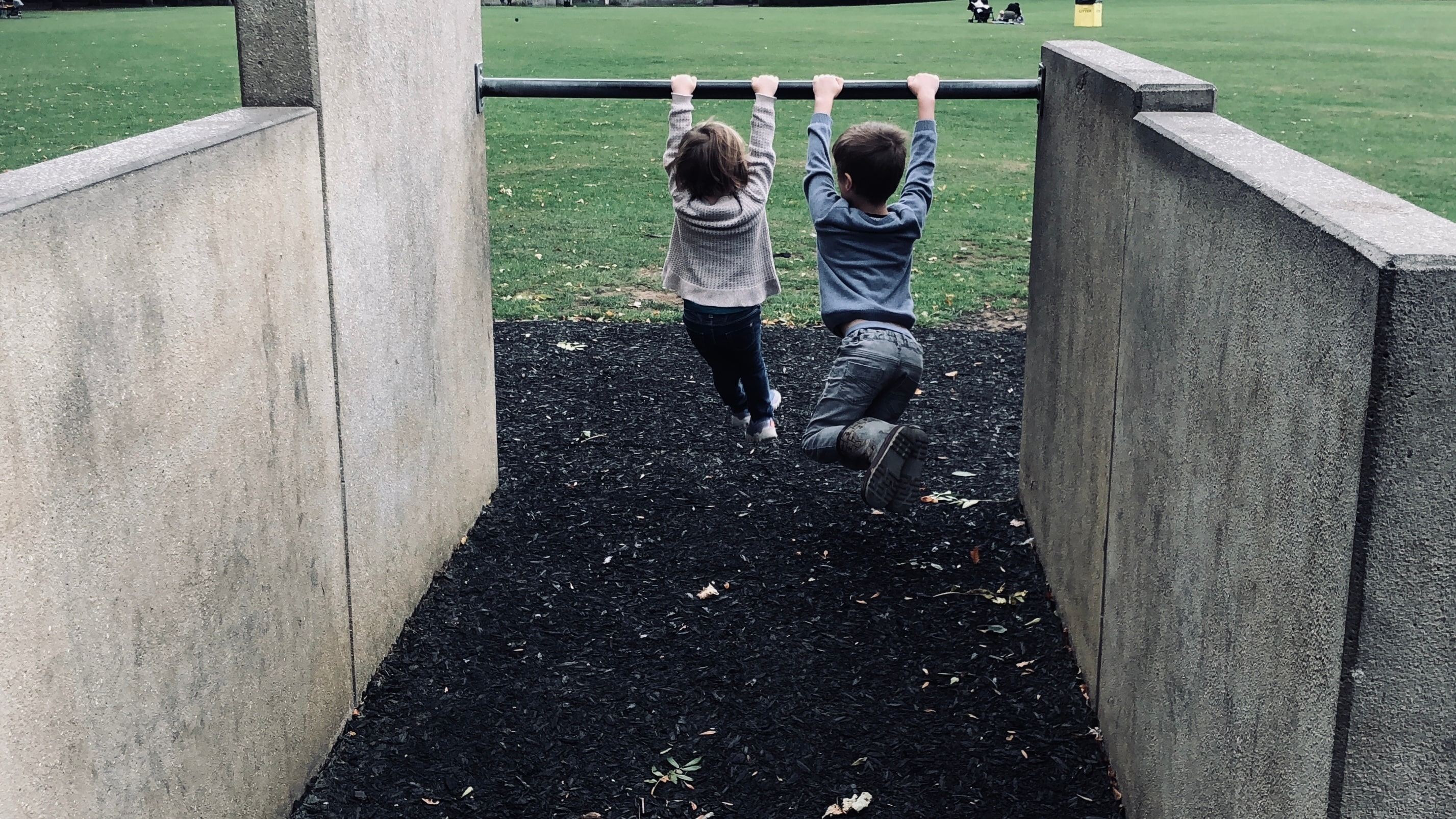 Two children hang from a metal bar on a playground.