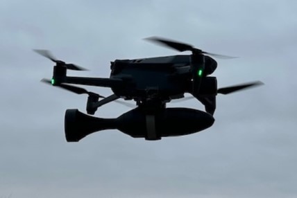 Black drone hovering in gray sky with green navigation lights