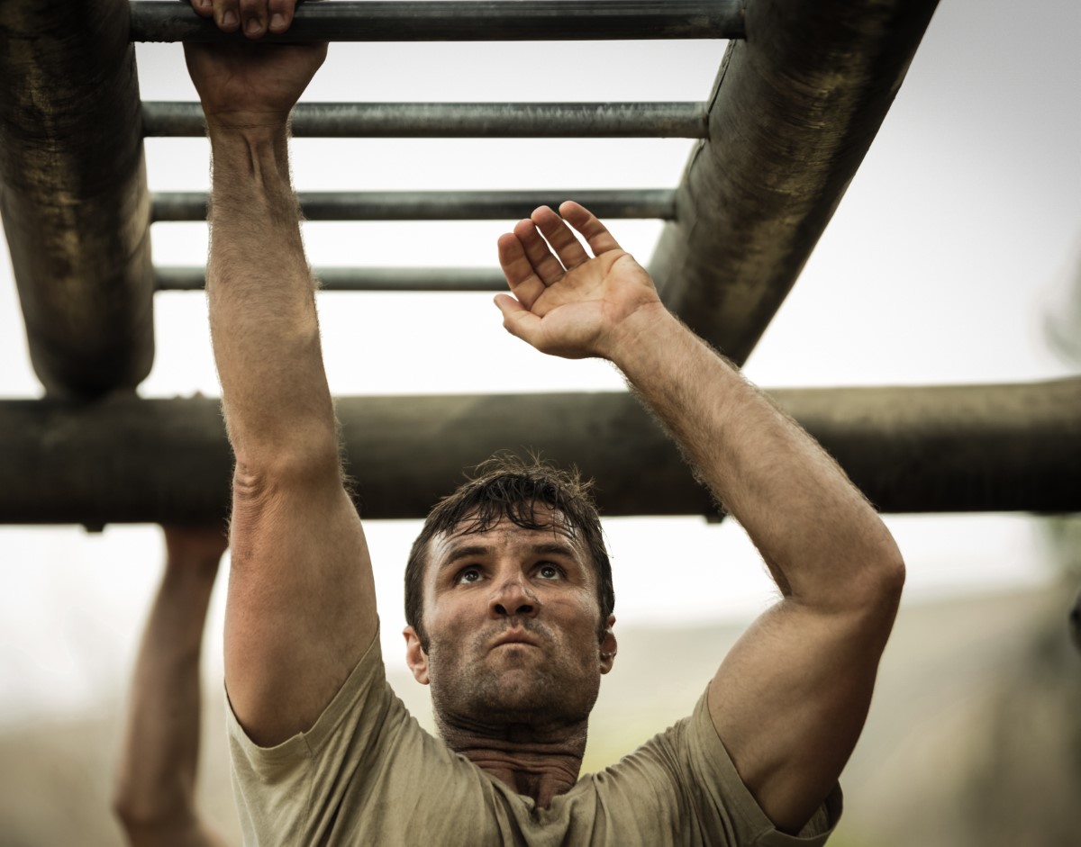 Athlete doing pull-ups on metal bar, sweating and focused during intense workout
