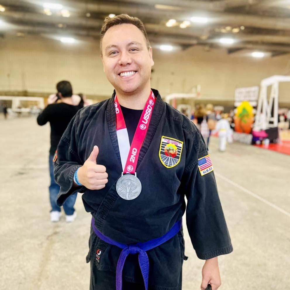Adult Karate Purple Belt Student smiling with a thumbs up after competition.