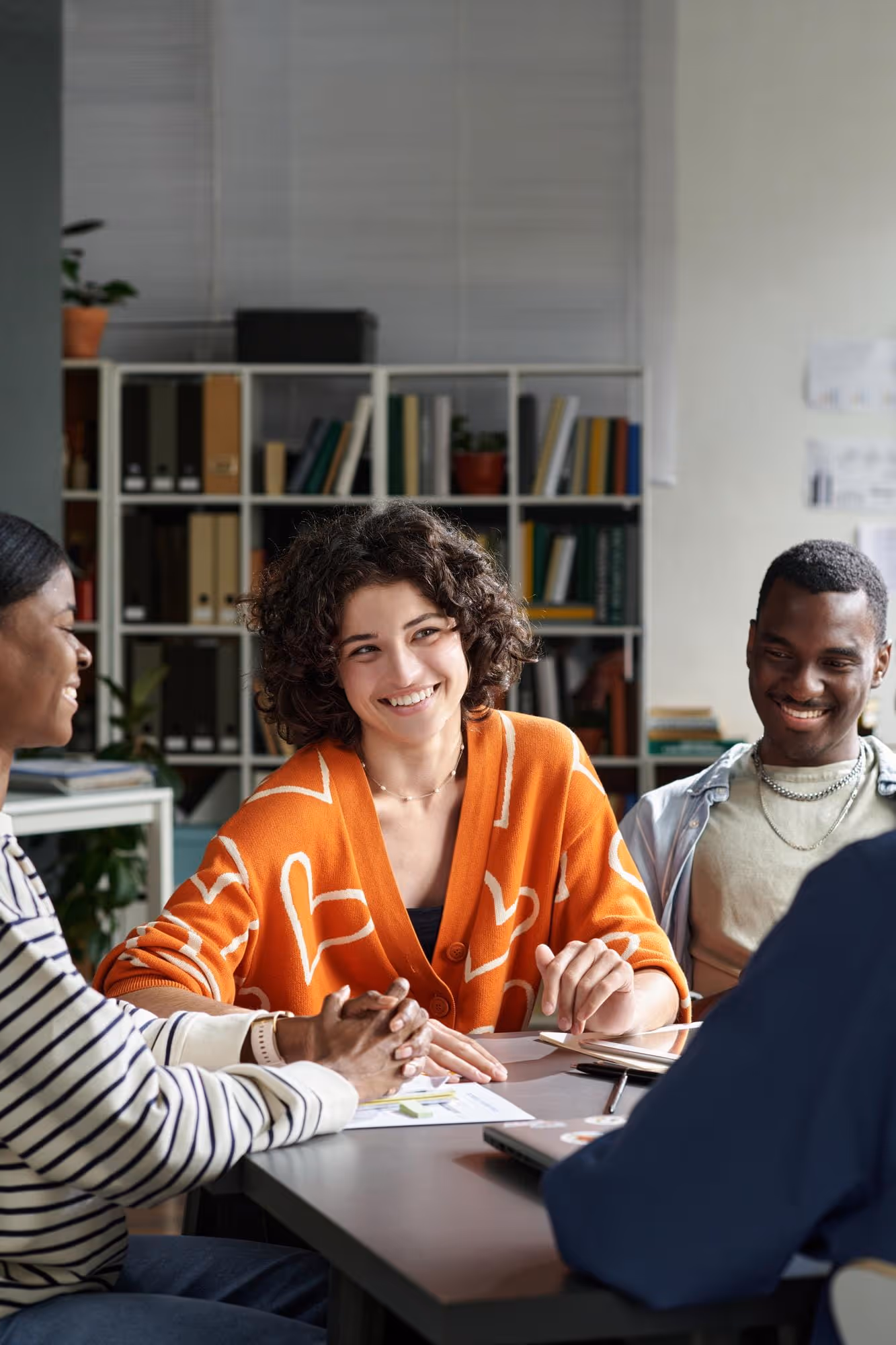 Four young adults sitting around a table smiling and engaging in a discussion in a bright office space.
