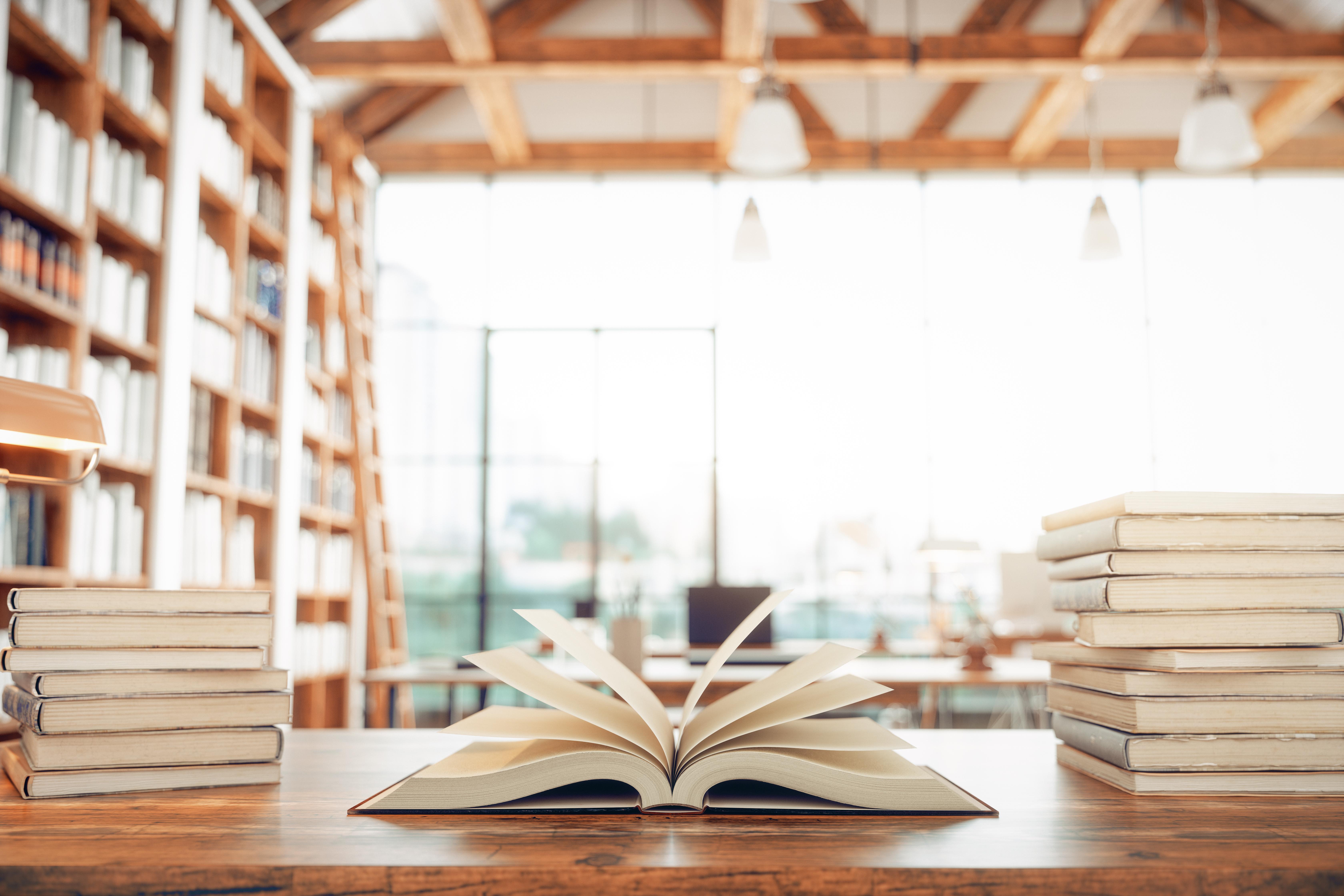 Open book on a library table surrounded by stacked books