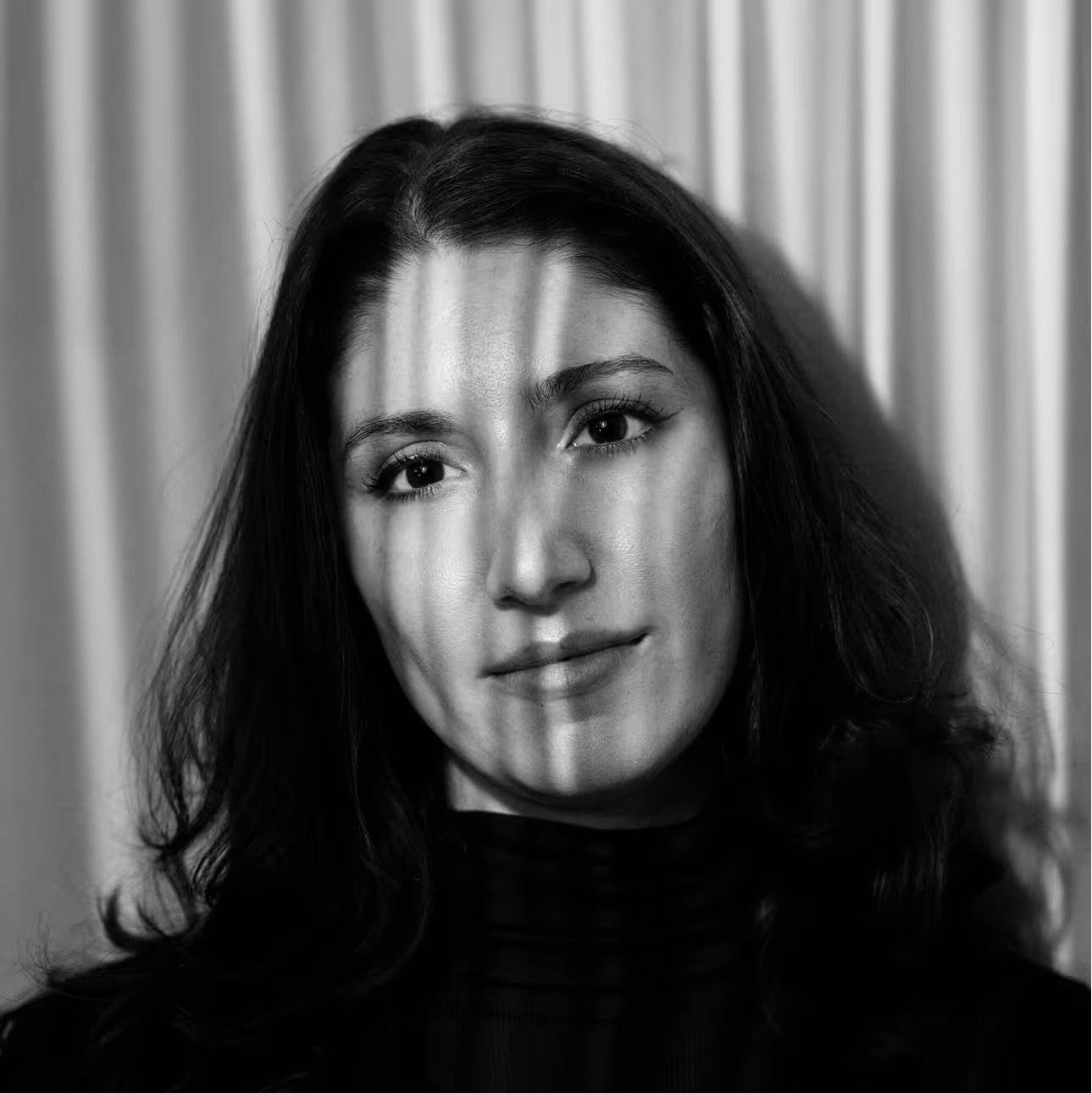 Black and white portrait of a woman with long hair lit by vertical shadows across her face.