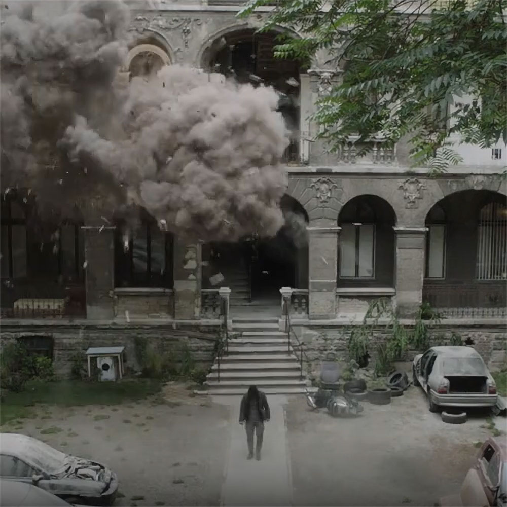 A man walks away from a building exploding behind him