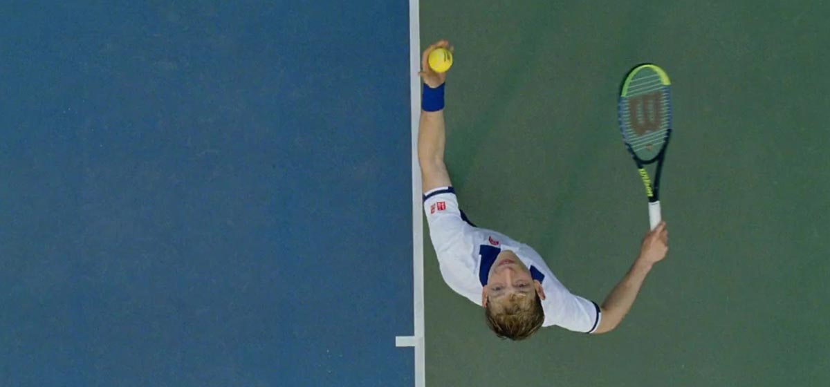 Looking directly down at a tennis player throwing a tennis ball above his head to serve