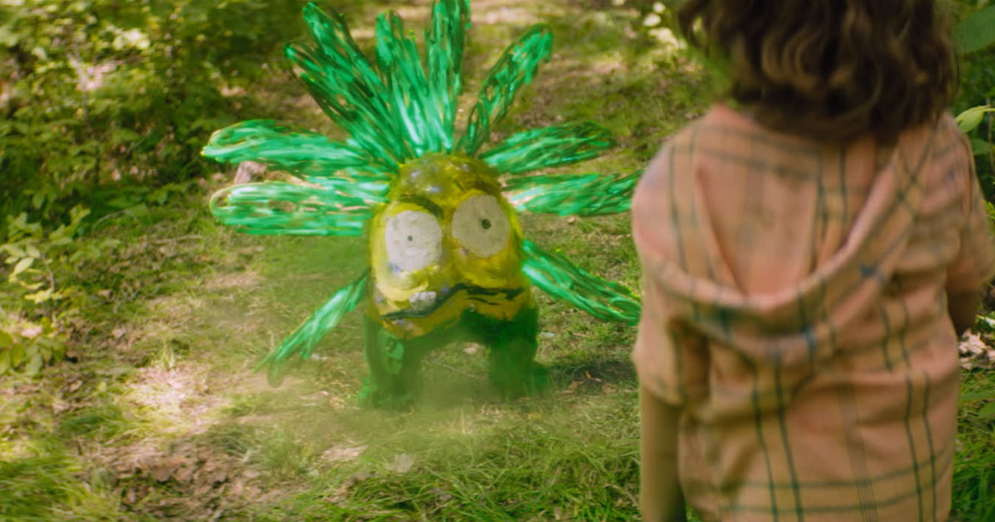 A young girl looks at a strange yellow and green creature that looks just like one of her drawings