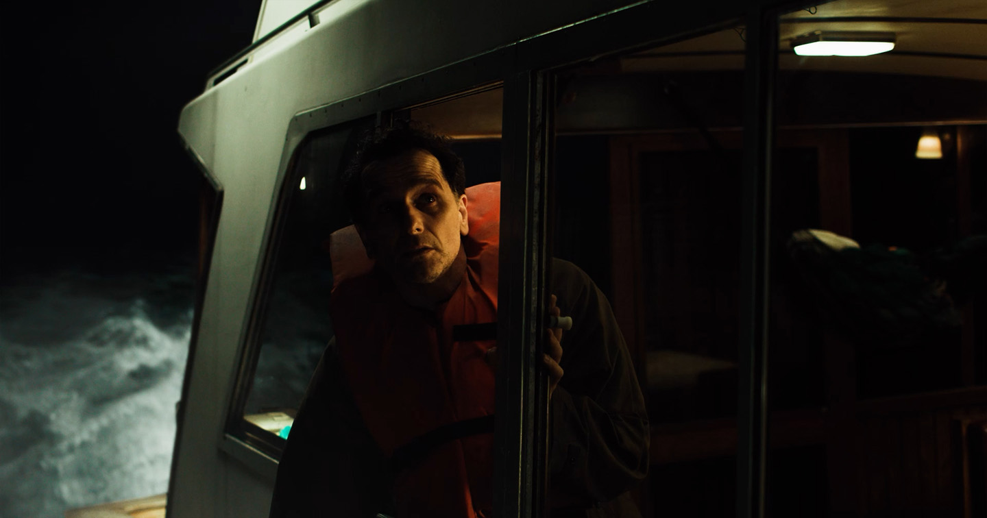 A man wearing a life vest looks out a boat window