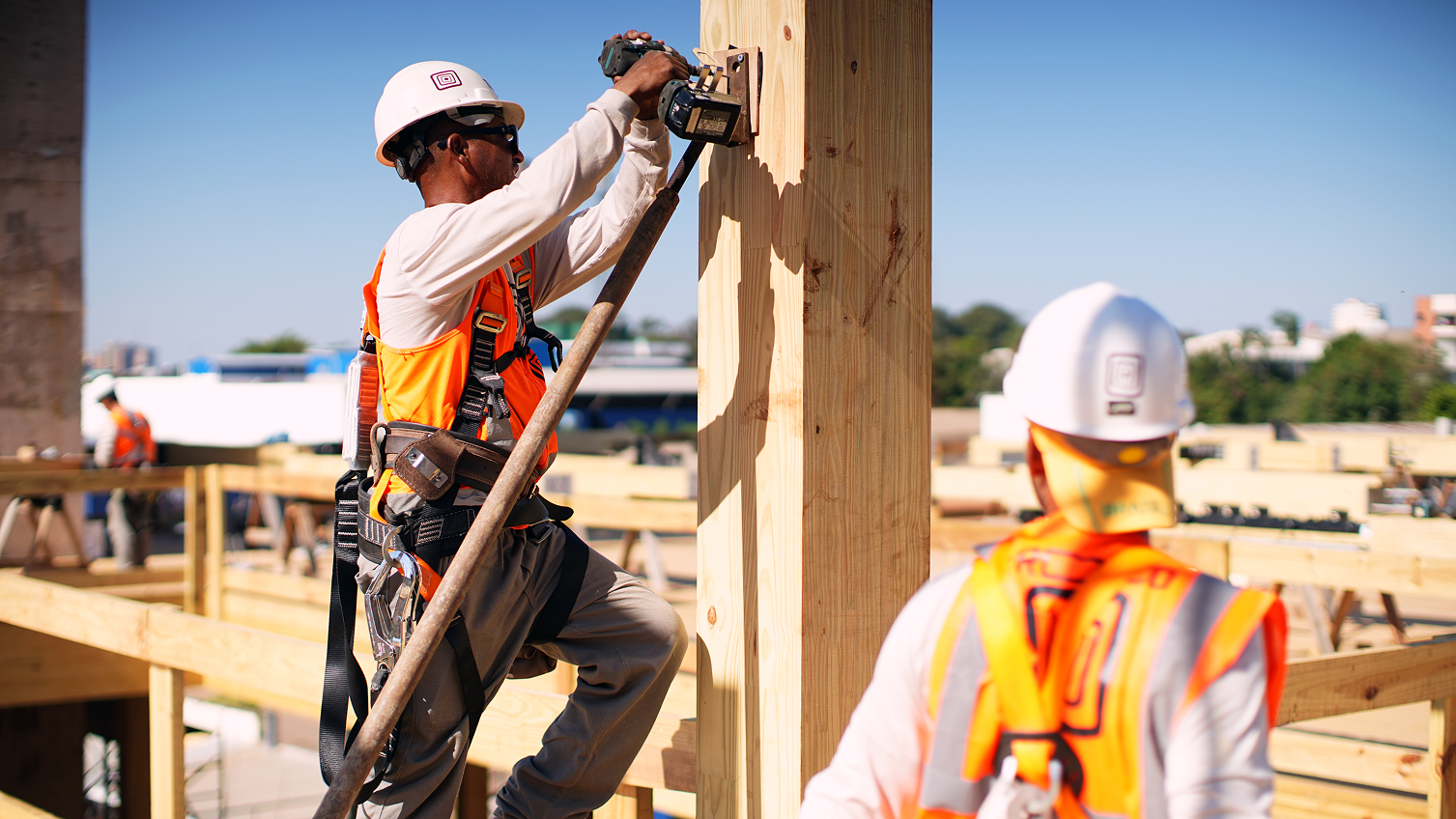 Dois trabalhadores de construção com coletes e capacetes instalando estrutura de madeira engenheirada.