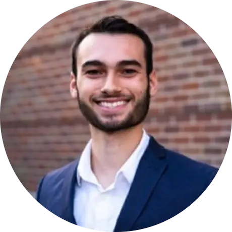 TeachFront team headshot of Kaden Semerad, smiling in a suit against a brick wall background.