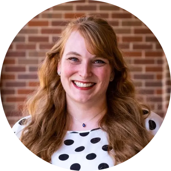 TeachFront testimonial headshot of Dr. Stephanie Valentine, smiling in front of a brick wall and wearing a black-and-white polka dot top.