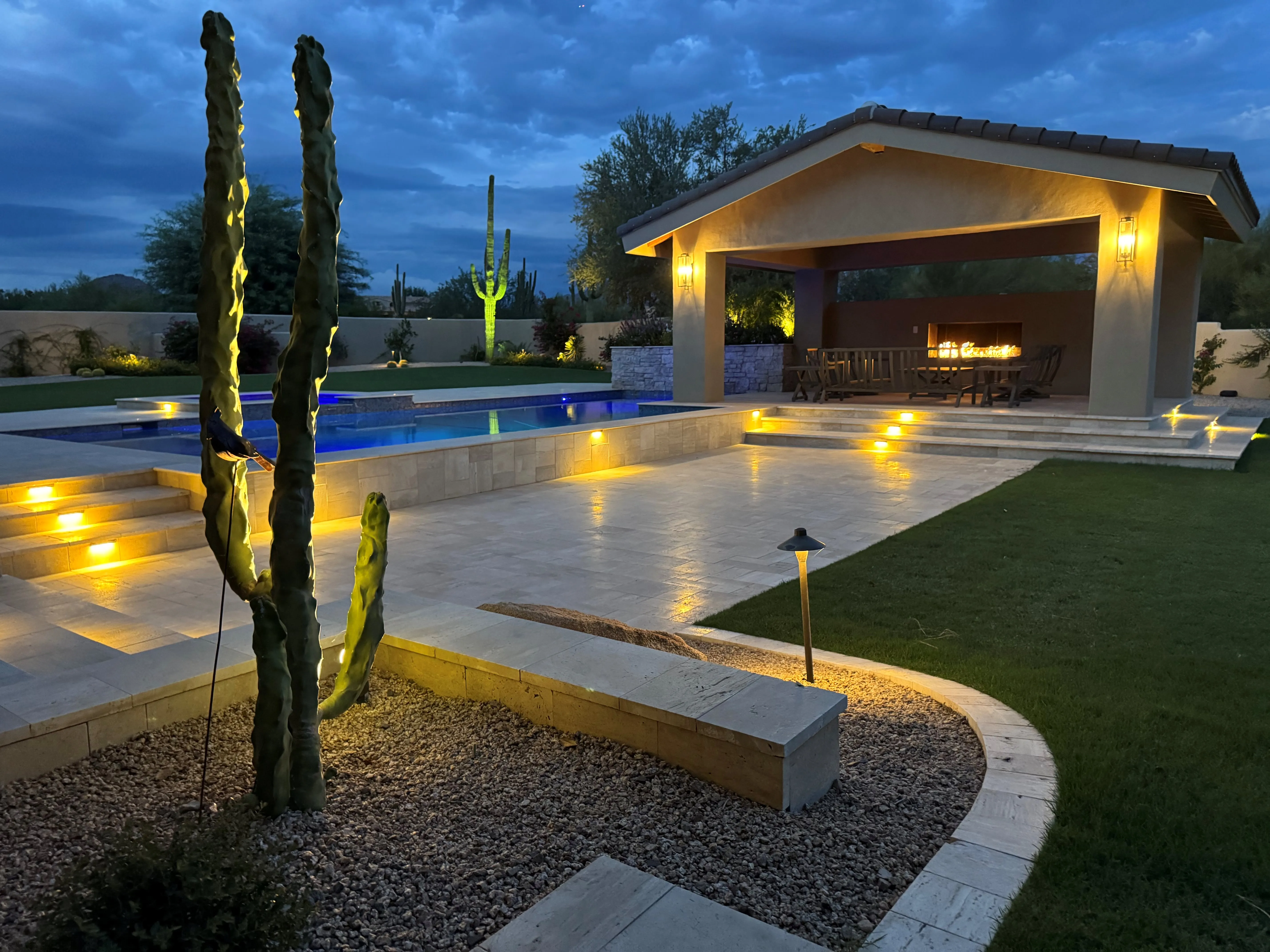 Resort‑style pool, ramada, and travertine patio with desert landscaping in Queen Creek, Arizona at dusk