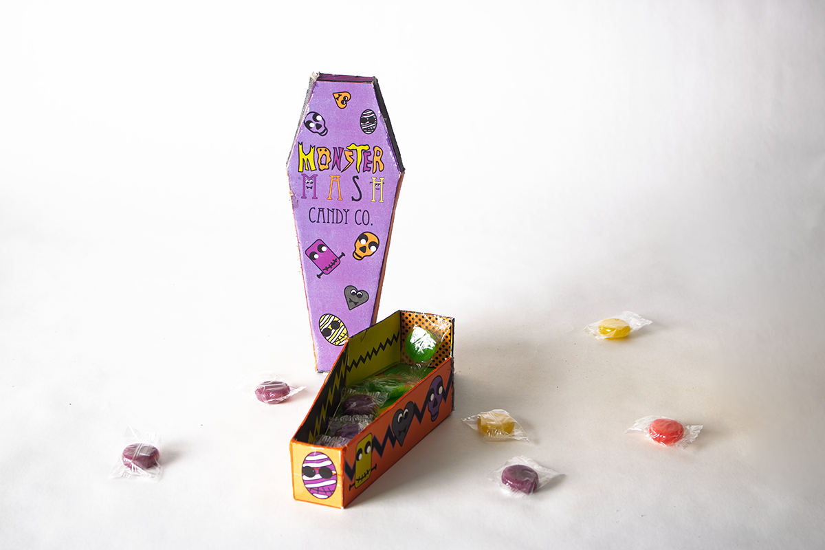 Coffin-shaped Monster Mash candy box with assorted wrapped candies on white background.