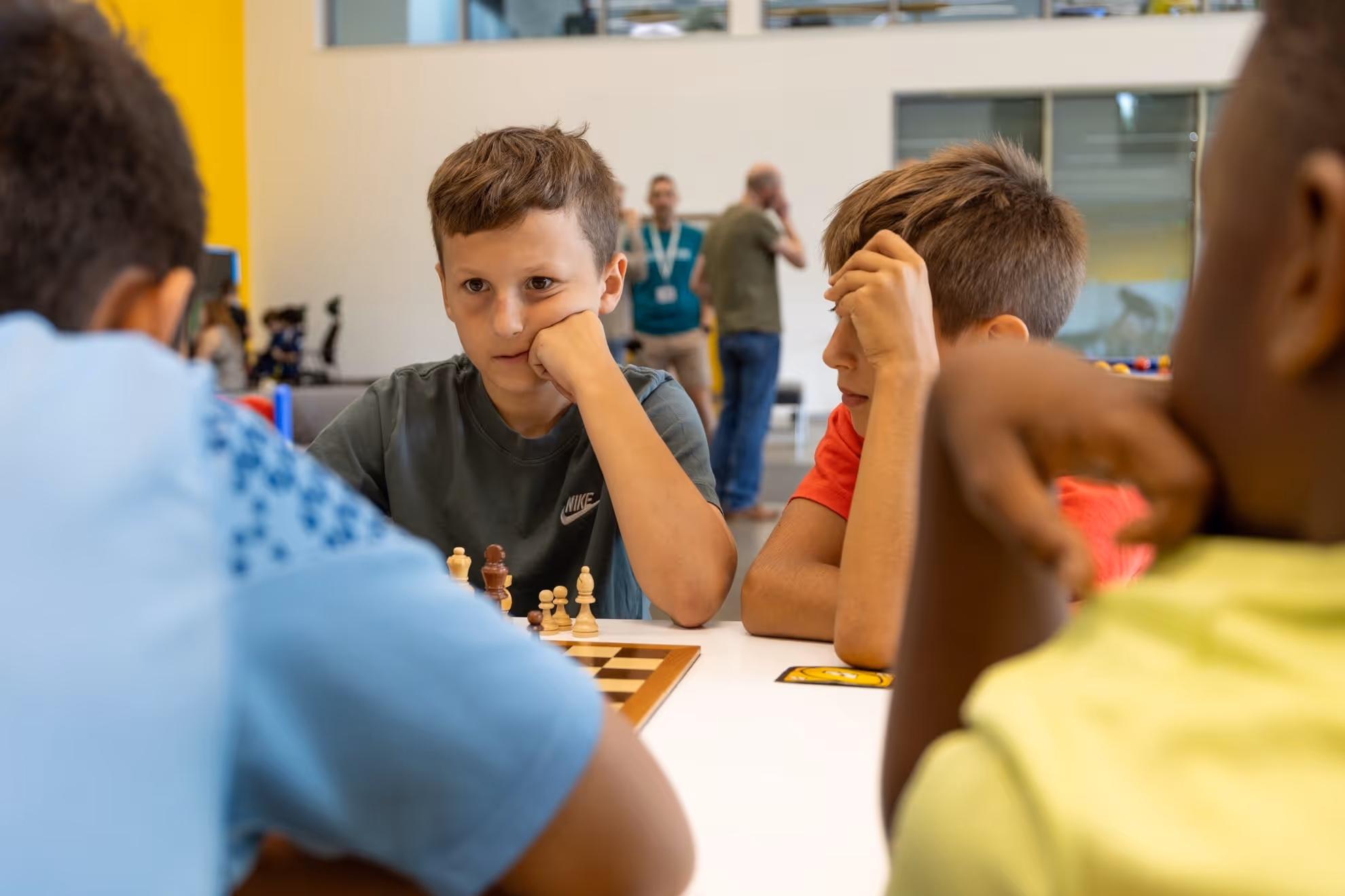 Four boys sitting around a table focused on a chess game indoors.