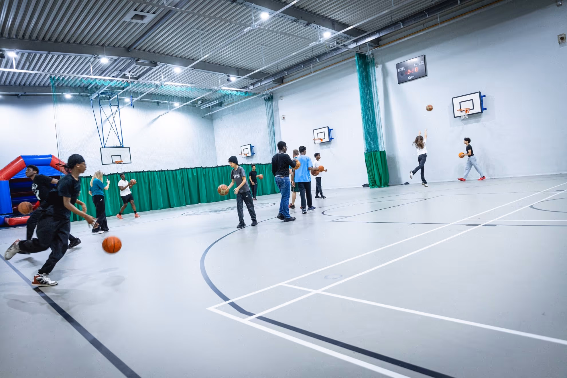 Group of young people practicing basketball shooting and dribbling in an indoor gymnasium.