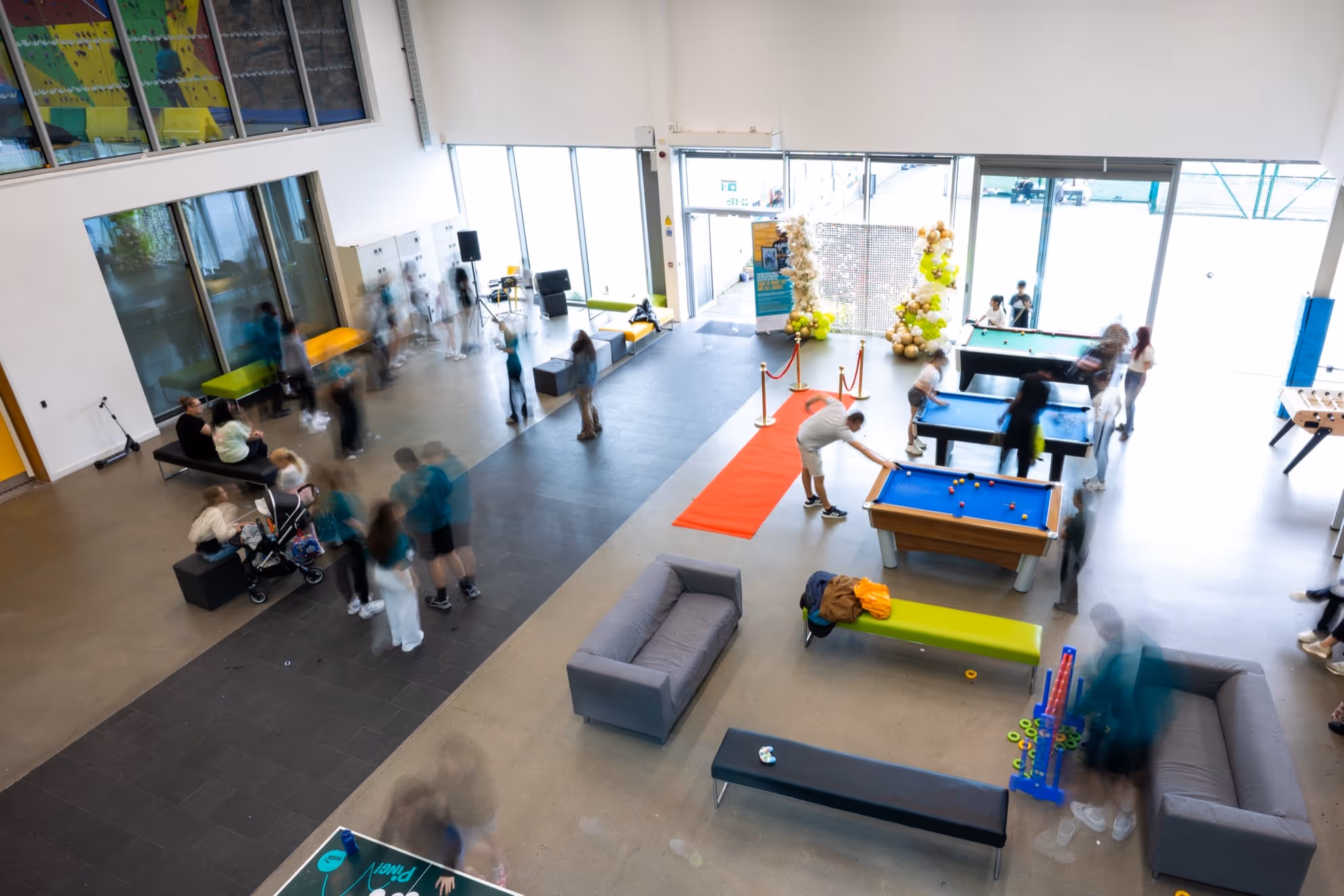 Indoor recreational area with people playing pool, sitting on couches and benches, and socializing in an open, modern space.