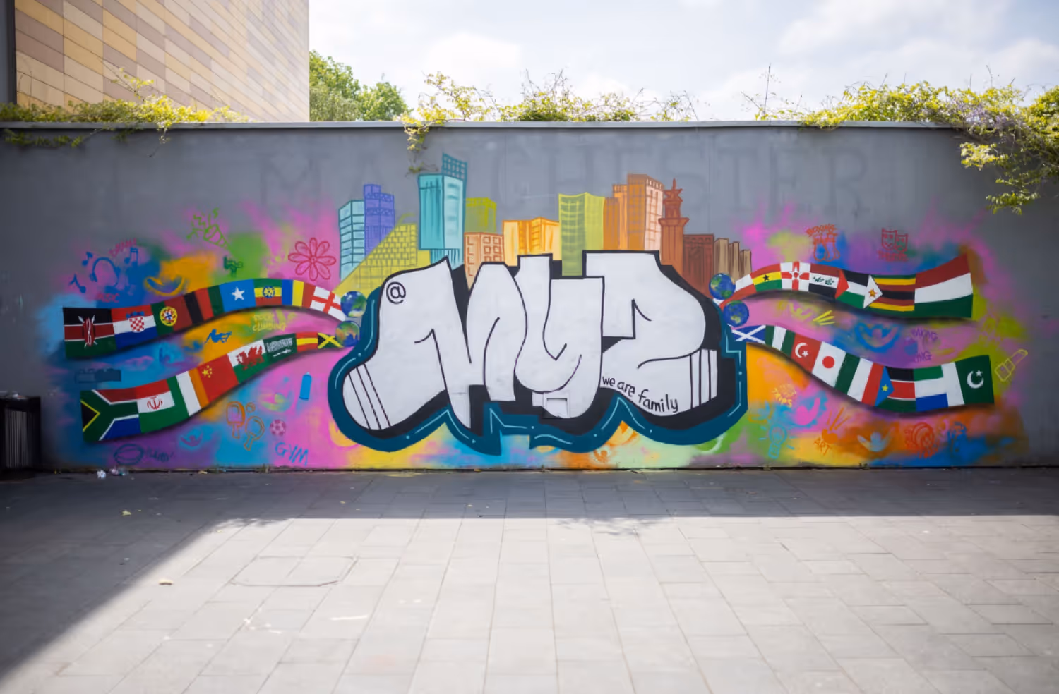Colorful graffiti mural with city skyline, international flags, and the word 'MYZ' with the phrase 'we are family' on a gray wall.