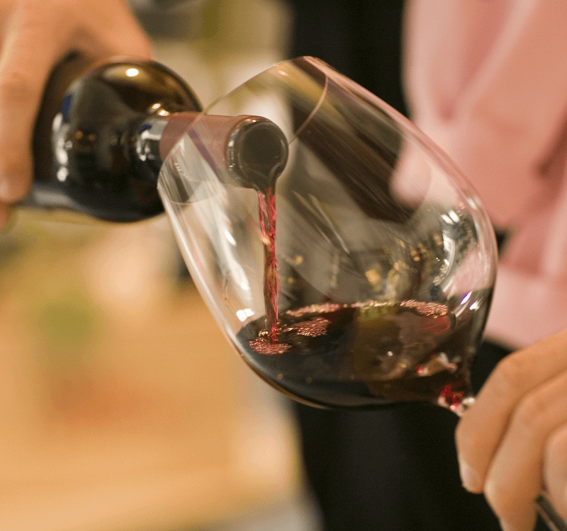 Person pouring red wine from bottle into a tilted wine glass.