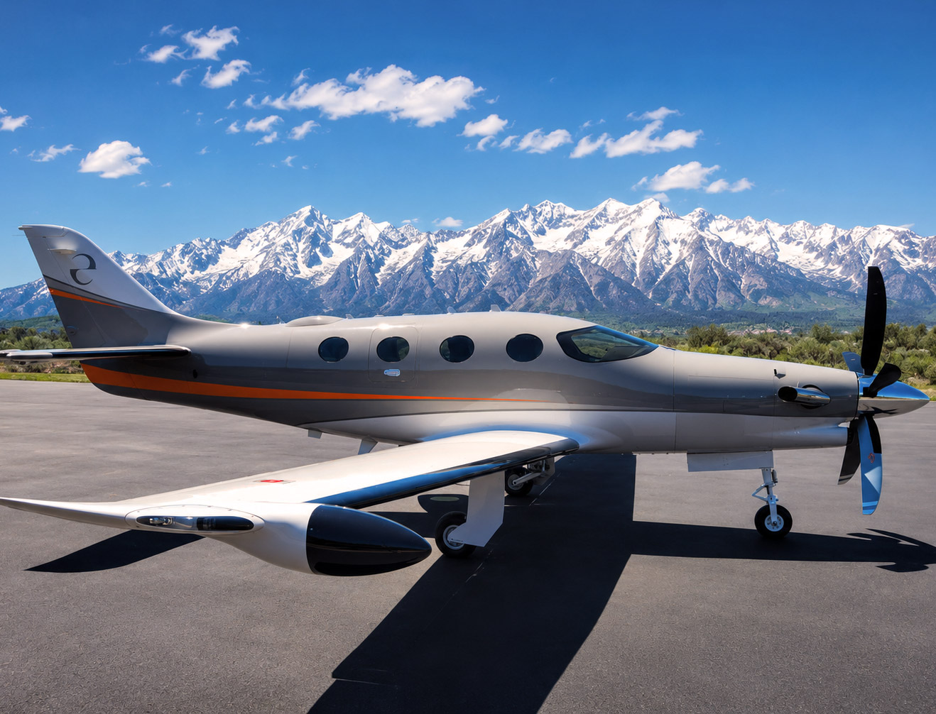 Small sleek airplane parked on tarmac with snow-capped mountains and blue sky in background.