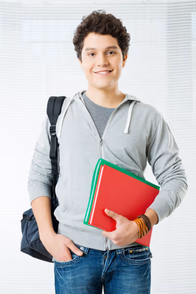Confident and happy male student holding text books and school bag.