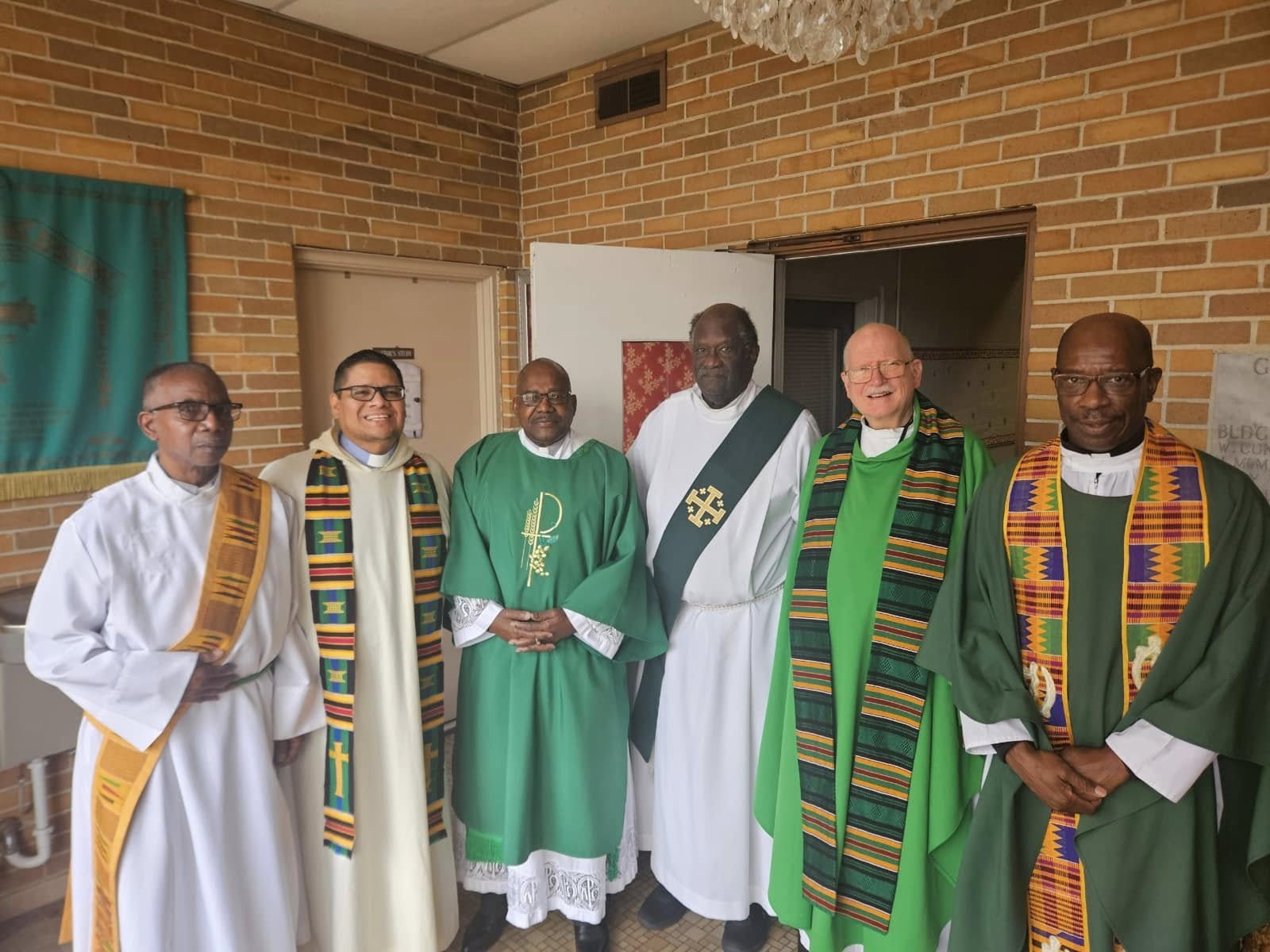 Three priests and two deacons stand together in their vestments following Mass at Holy Family Cristo Rey Catholic High School