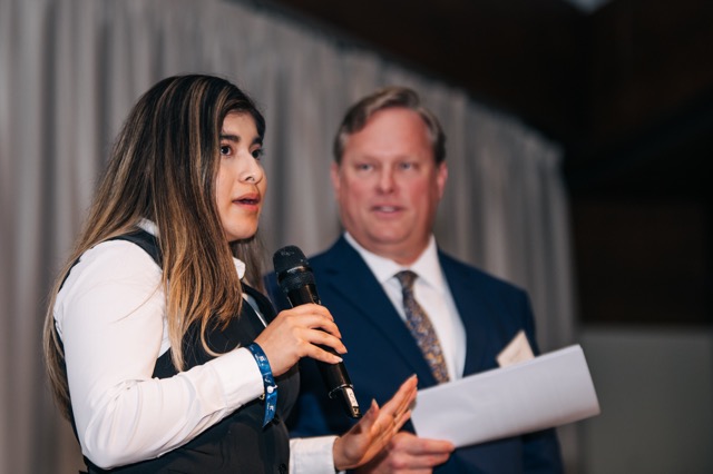 A Holy Family Cristo Rey student standing next to the school's president speaks to the crowd at the 2025 Rey of Hope Gala