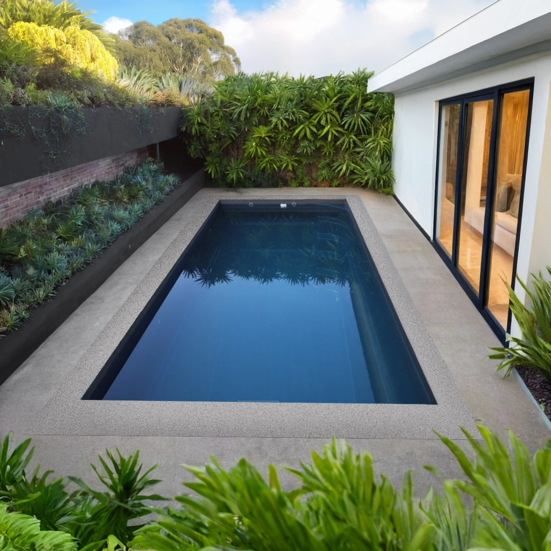 Modern rectangular backyard pool with blue water surrounded by plants and a white house with glass doors.