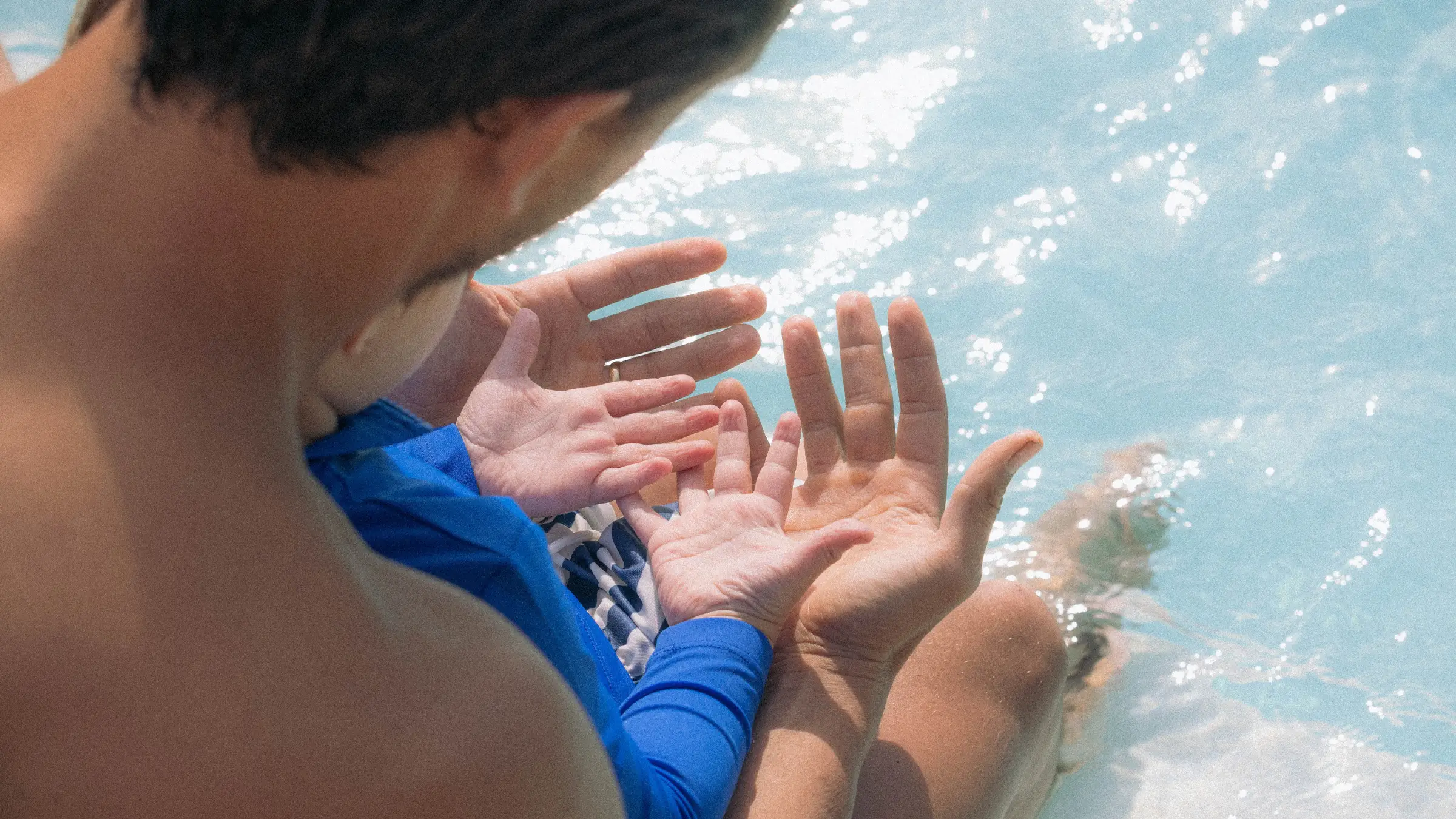 Adult and child sitting by a pool, showing their outstretched hands over the water.