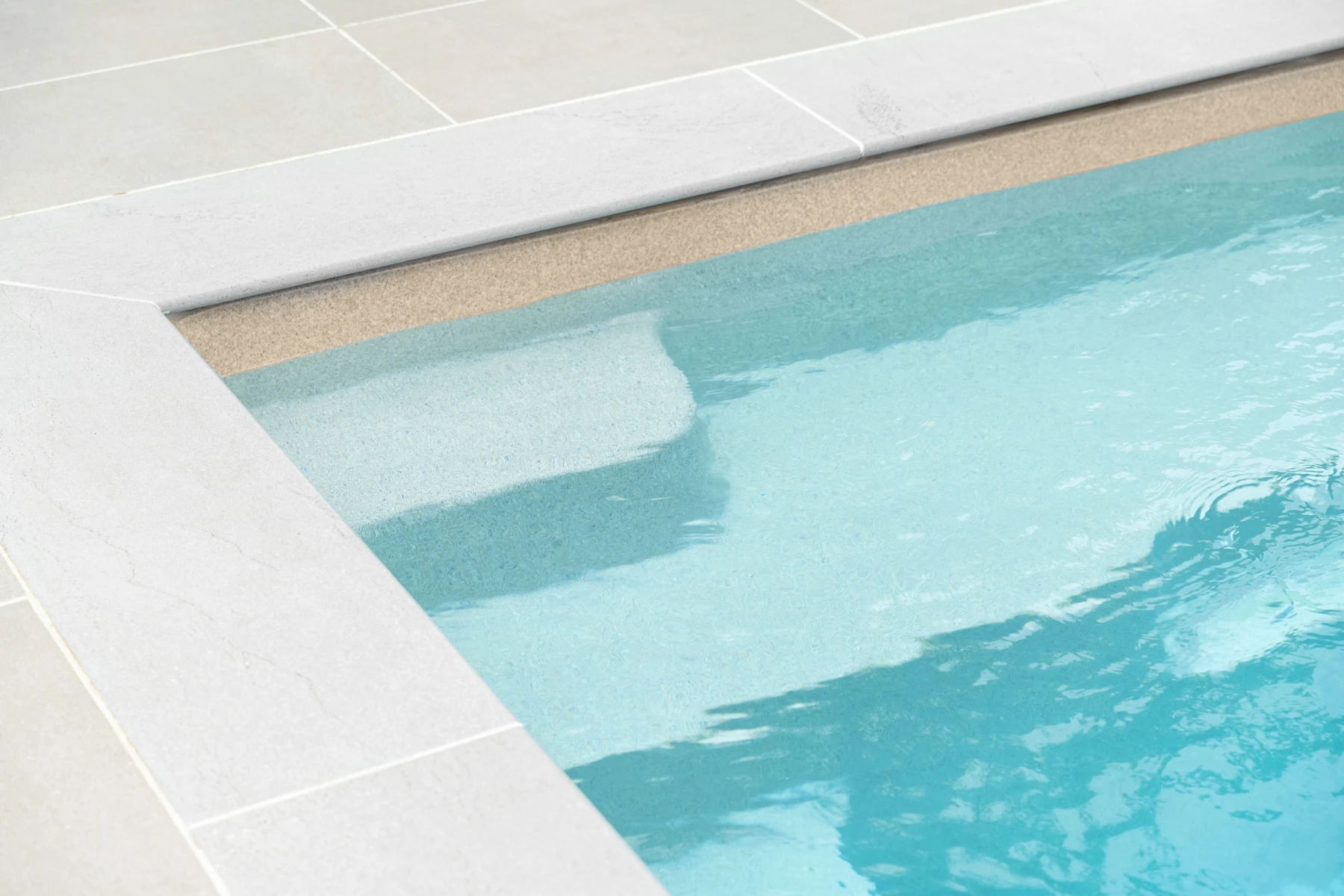 Close-up of a sandstone-colored fiberglass pool edge with clear blue water and beige pool interior.