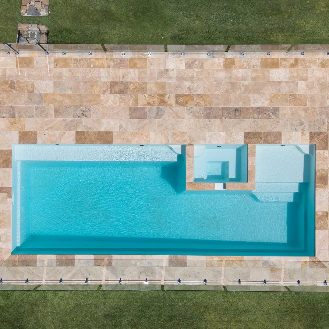 Top view of Peninsula swimming pool with built-in spa and steps, surrounded by stone tiles and grass.