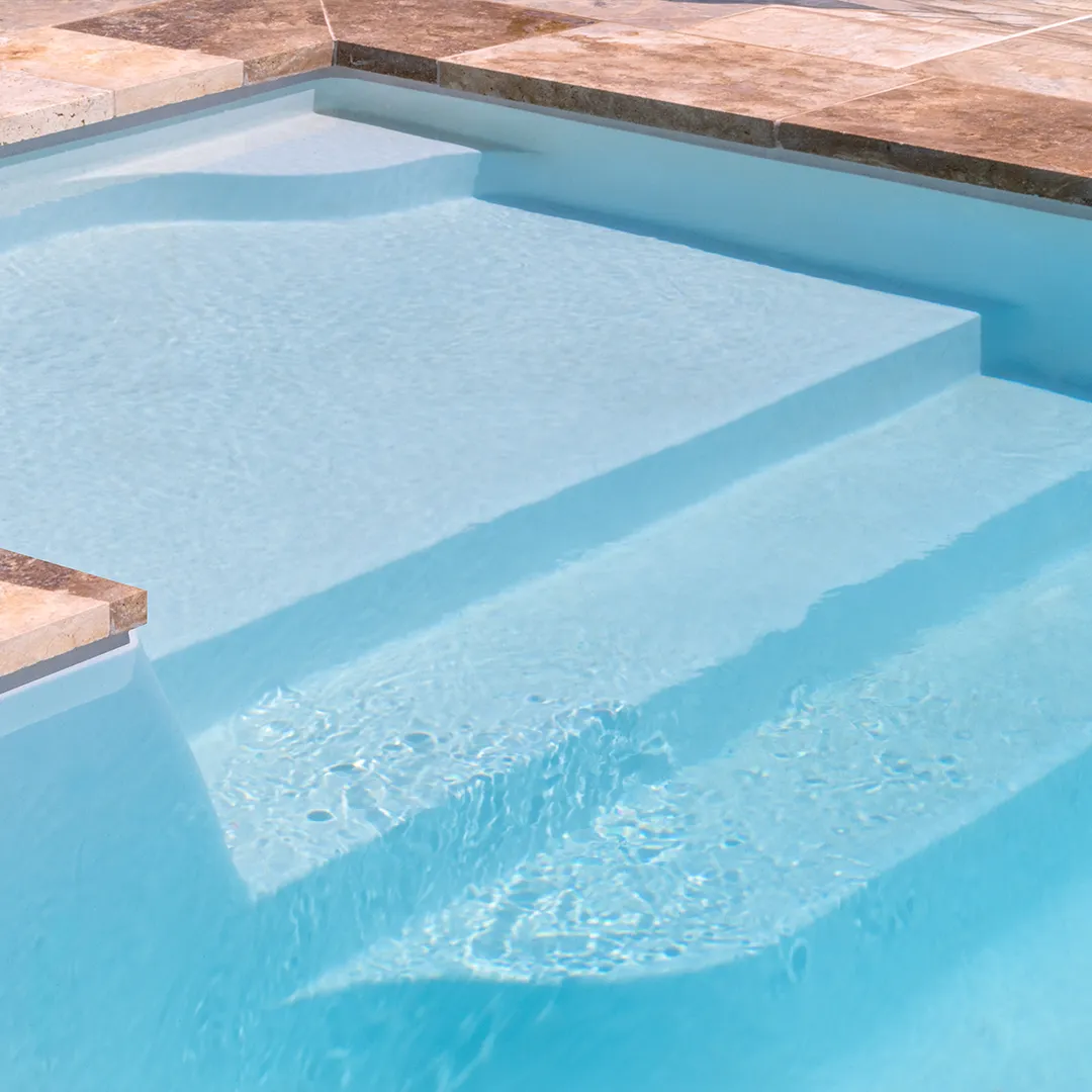 Close-up of clear Peninsula pool steps with textured stone pool deck around the edge.