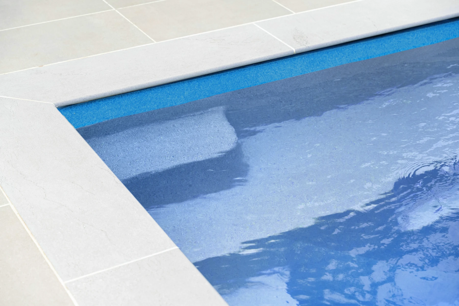 Close-up of a mid-blue fiberglass pool with light-colored stone tiles around the edge.