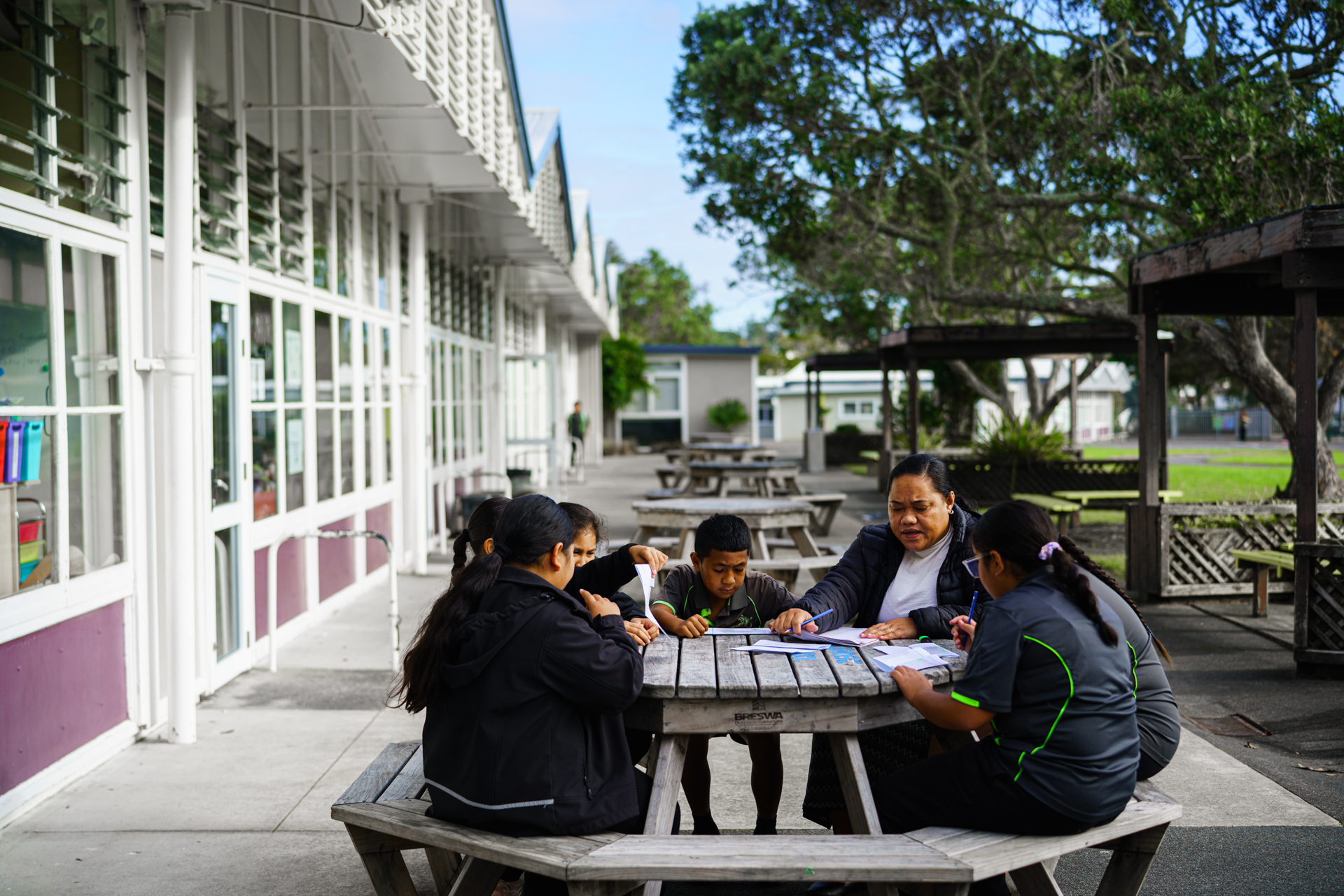 Students sit outside doing their work with a teacher.