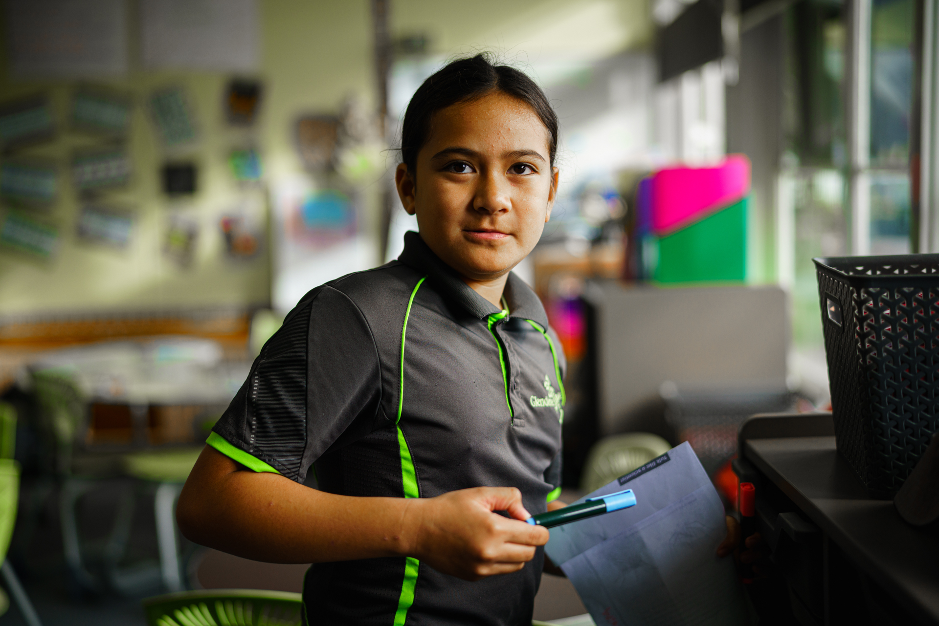 Young student looks beyond the camera, holding a pen and paper.