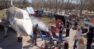 People working around a private jet on a tarmac with equipment and vehicles nearby.