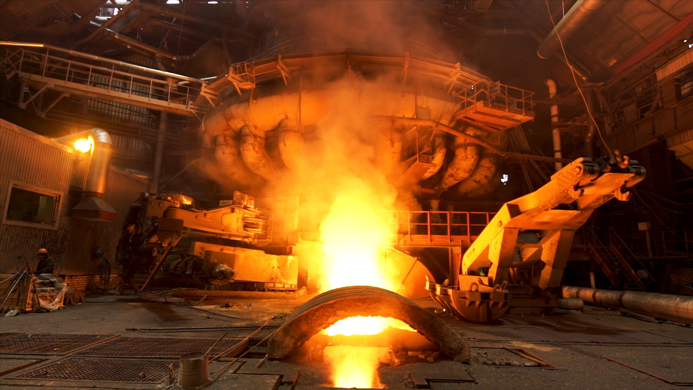 Molten metal pouring from a furnace in a glowing industrial steel foundry.