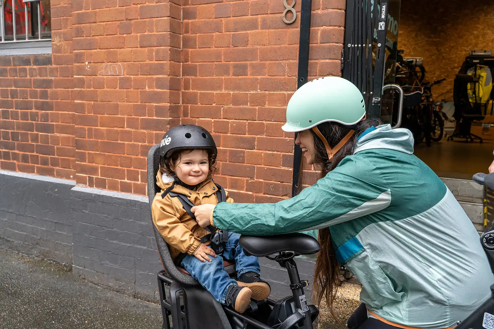 A parent straps a helmet on a child in a Zoomo Family cargo e-bike child seat in Melbourne.
