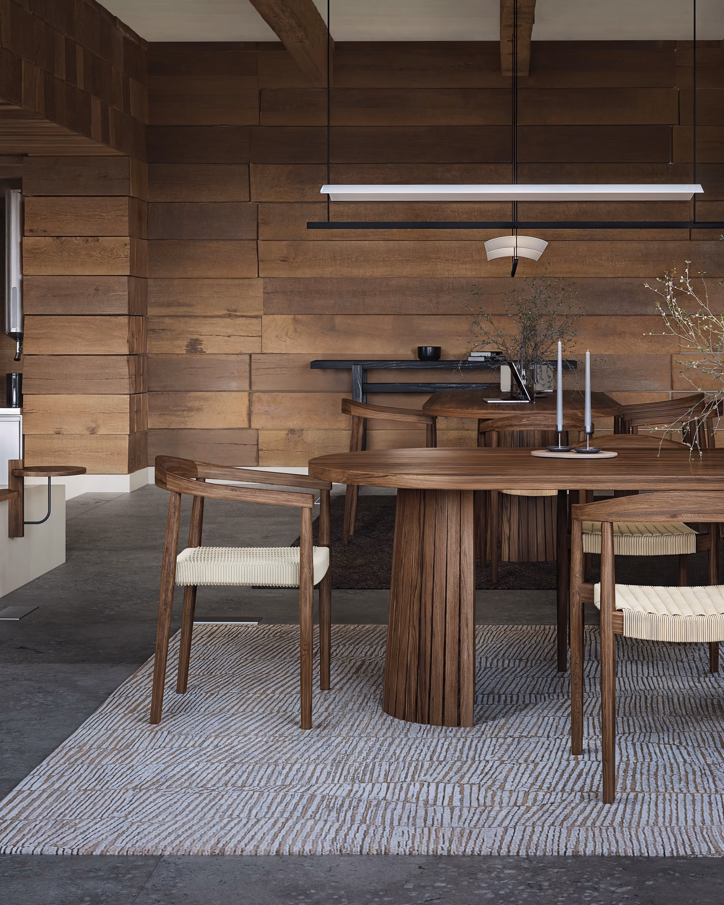 Nowoczesna jadalnia z owalnym drewnianym stołem, krzesłami z plecionymi jasnymi siedziskami i drewnianymi panelami ściennymi.