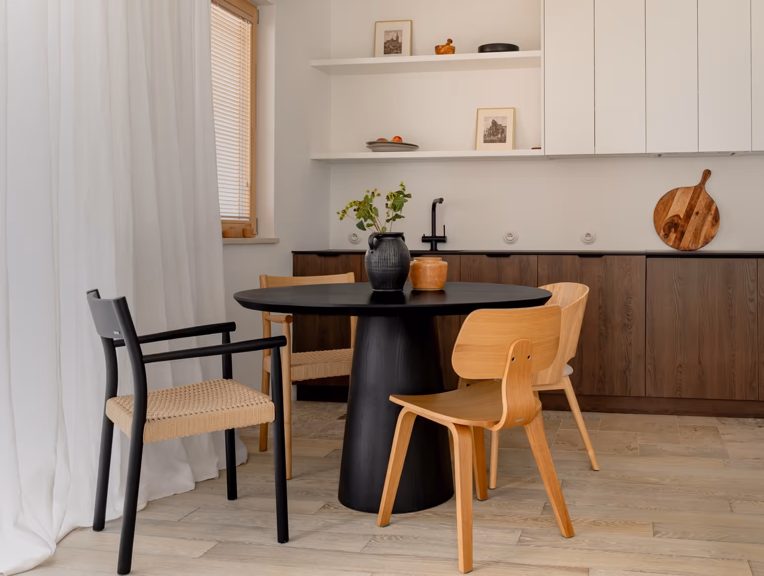 Nowoczesny czarny okrągły stół w kuchni z mieszanką drewnianych i czarnych krzeseł oraz wazonem z zielonymi liśćmi.