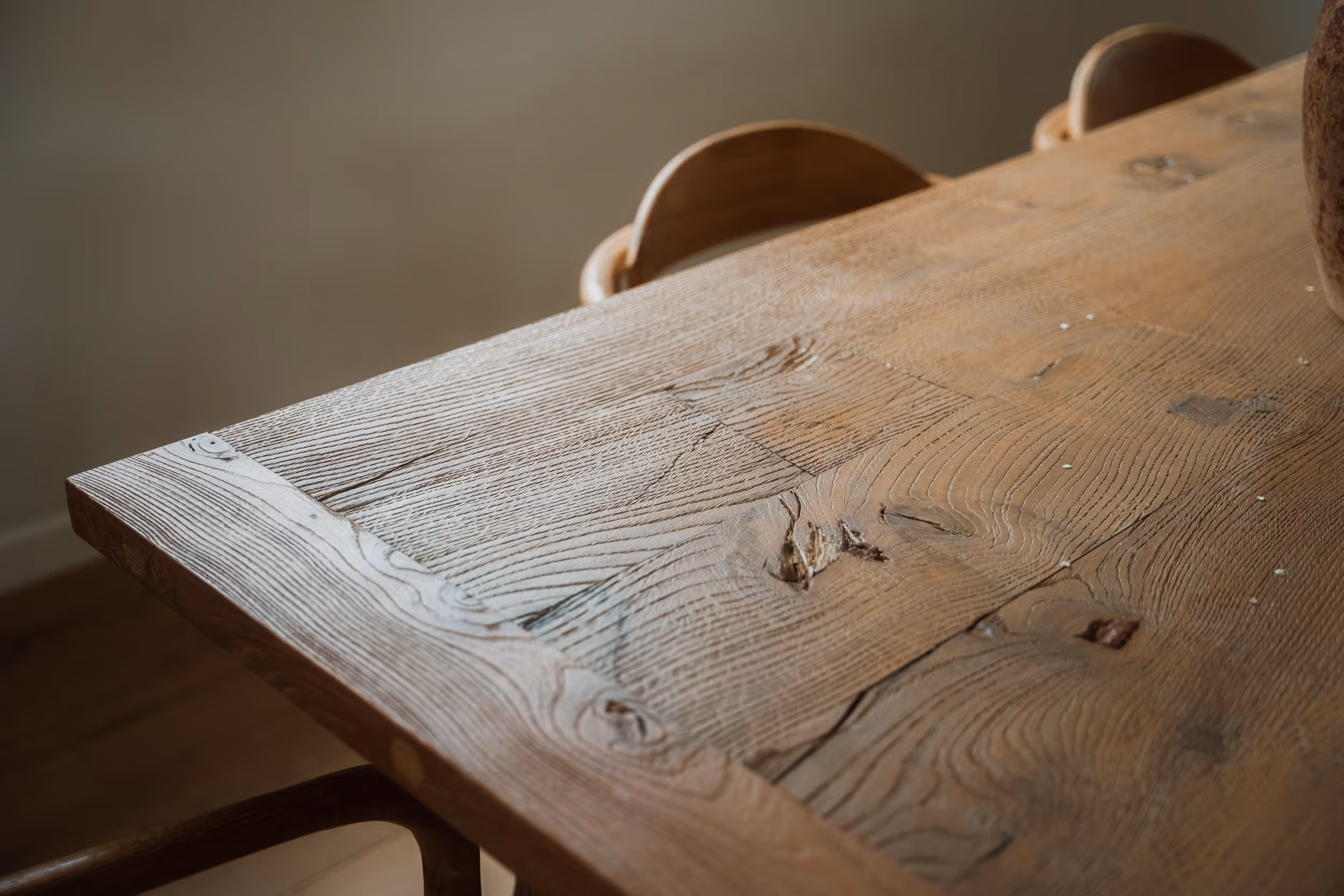 Stół z naturalnego drewna z widocznym usłojeniem i kilkoma drewnianymi krzesłami w tle.