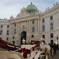 Pferdekutschen vor der historischen Hofburg in Wien mit grün-goldener Kuppel im Hintergrund.