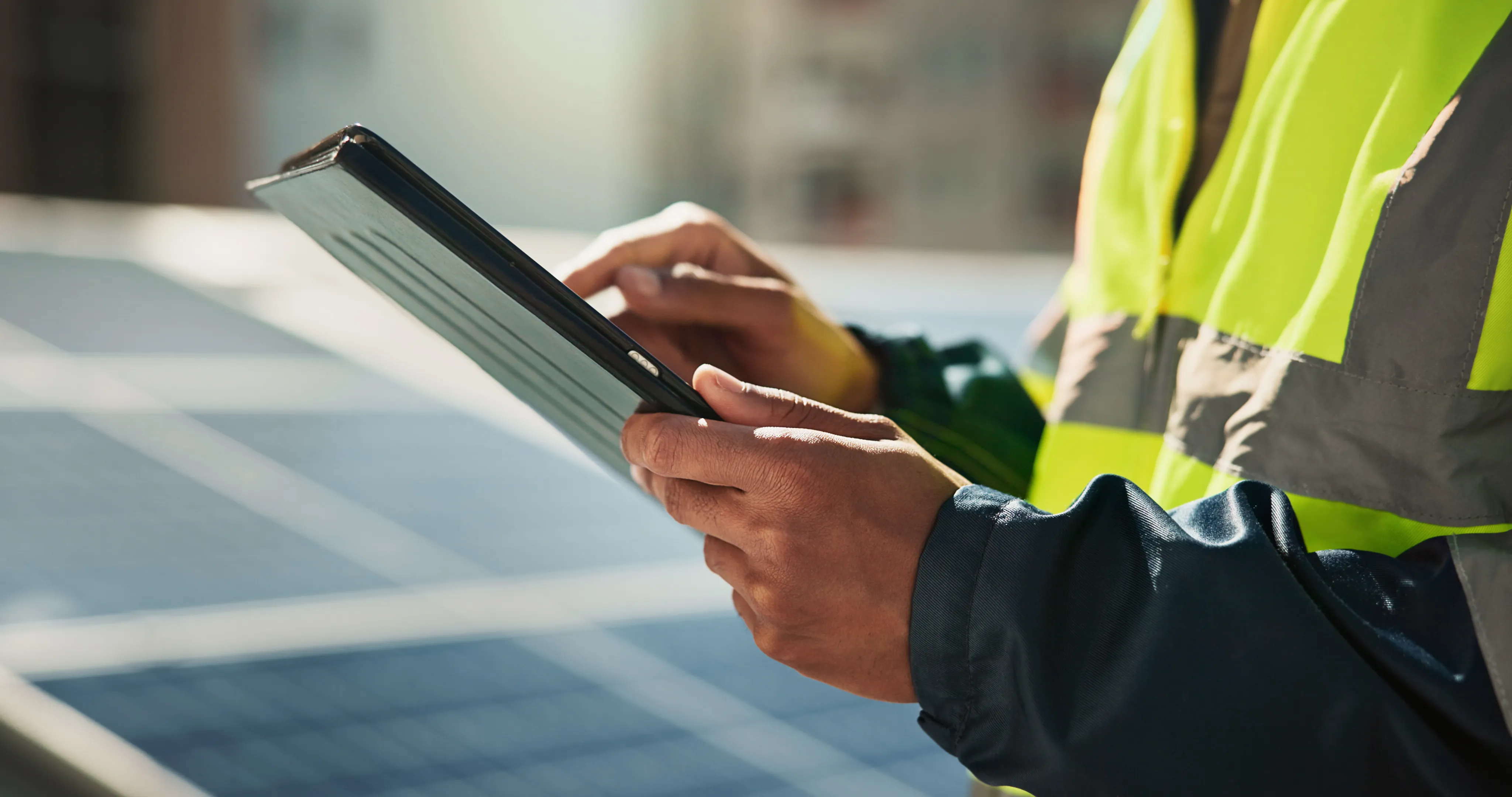 Person in a reflective safety vest using a tablet with solar panels in the background.
