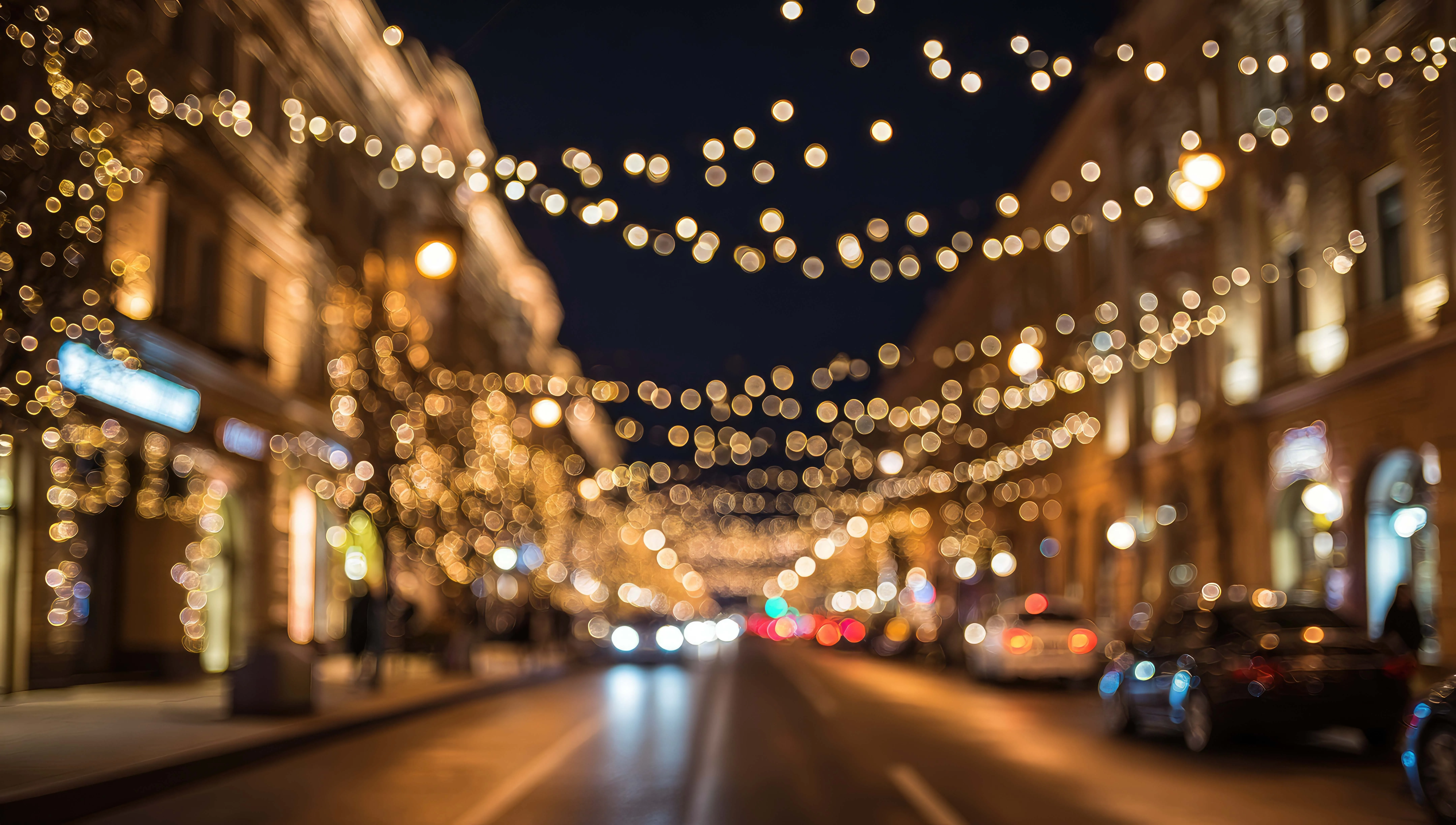 Verschwommene Straßenansicht bei Nacht mit festlichen Lichterketten über der Fahrbahn und beleuchteten Gebäuden.