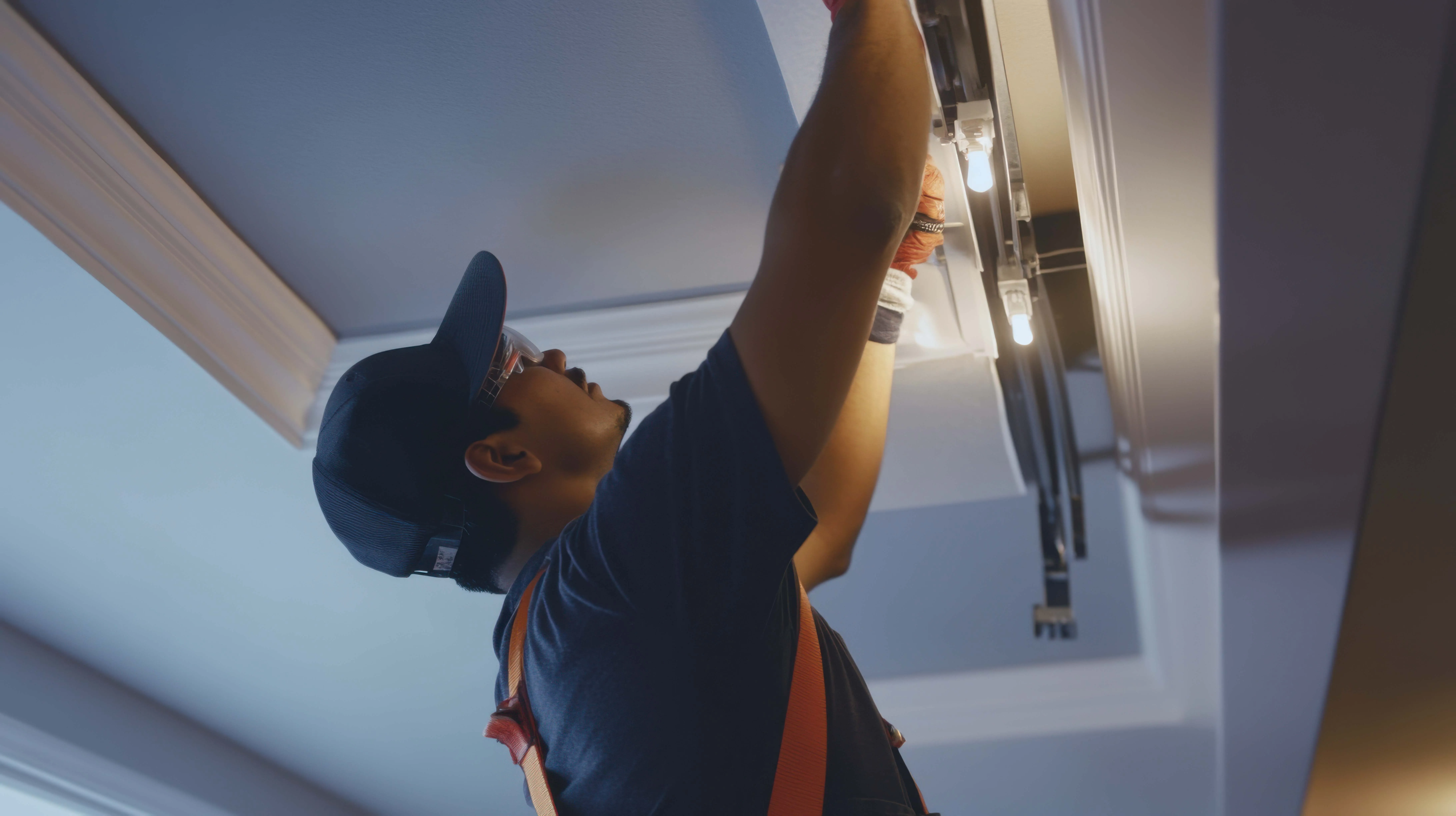 Elektriker mit Schutzbrille und Kappe installiert oder repariert eine Deckenleuchte in einem Raum.