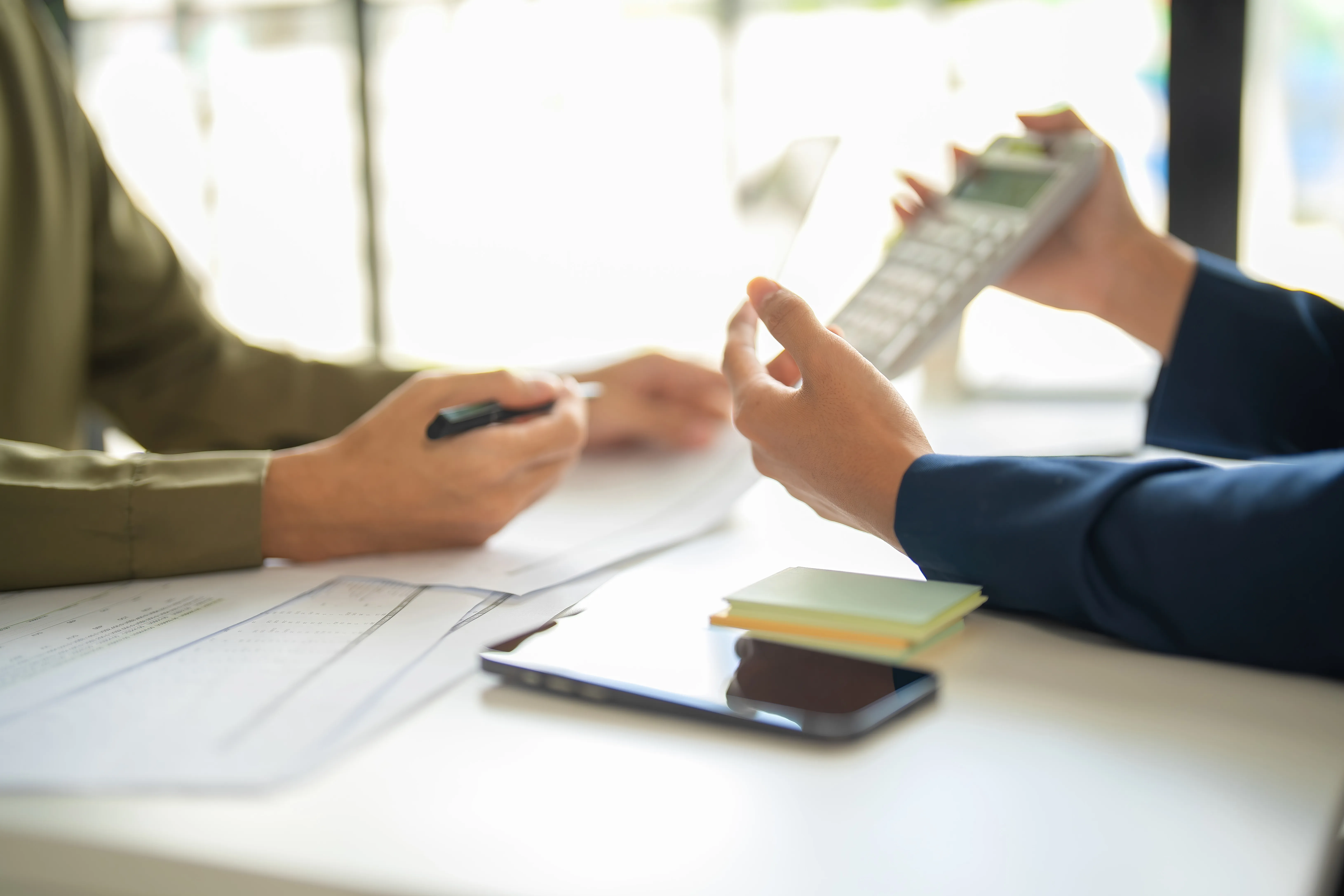 Zwei Personen beim Berechnen mit Taschenrechner und Überprüfung von Dokumenten am Schreibtisch.