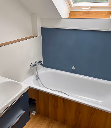 Modernes Badezimmer mit Badewanne, blauer Wandverkleidung, Holzfront und Oberlichtfenster.