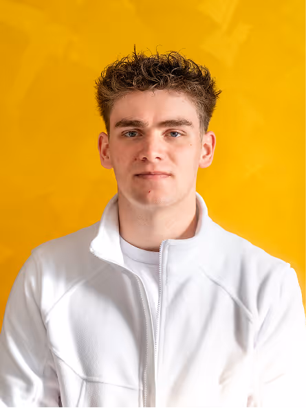 Junger Mann mit lockigem Haar trägt weiße Jacke vor gelbem Hintergrund.