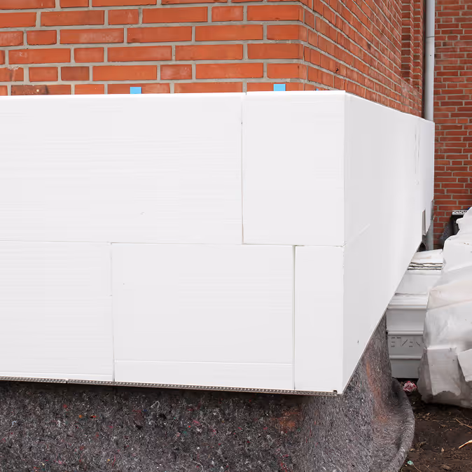 Weiße Dämmplatten an einer Hauswand aus roten Ziegeln, die Ecke eines Gebäudes zeigend.