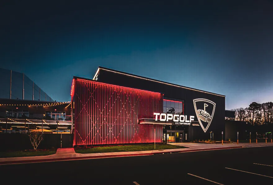 Topgolf venue at night with red-illuminated exterior and dark blue sky